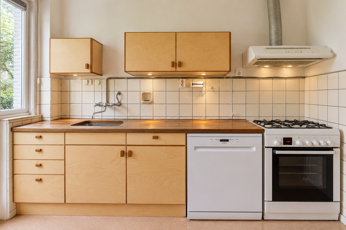 Keuken vóór renovatie met lichte houten kasten, witte wandtegels en een vrijstaand gasfornuis
