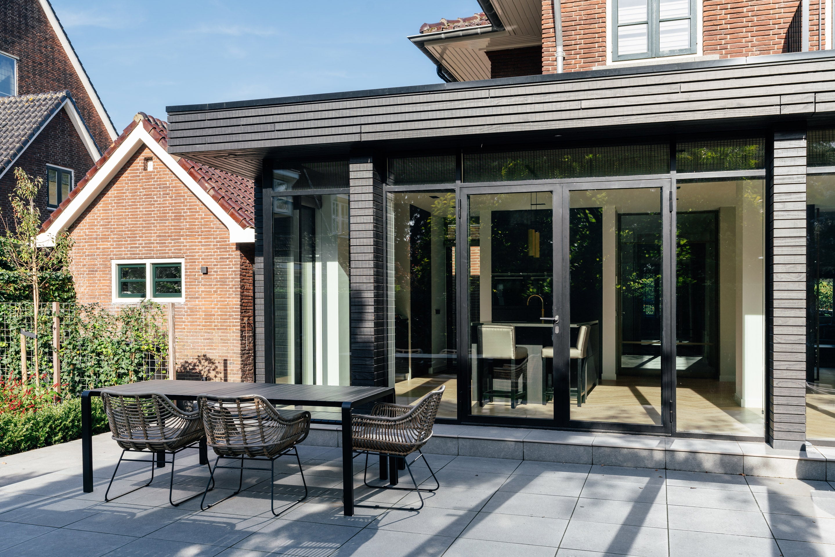 Tuinzijde van een karakteristieke jaren '30 woning met een moderne uitbreiding, veel daglicht en een ruim buitenterras in directe verbinding met de keuken.