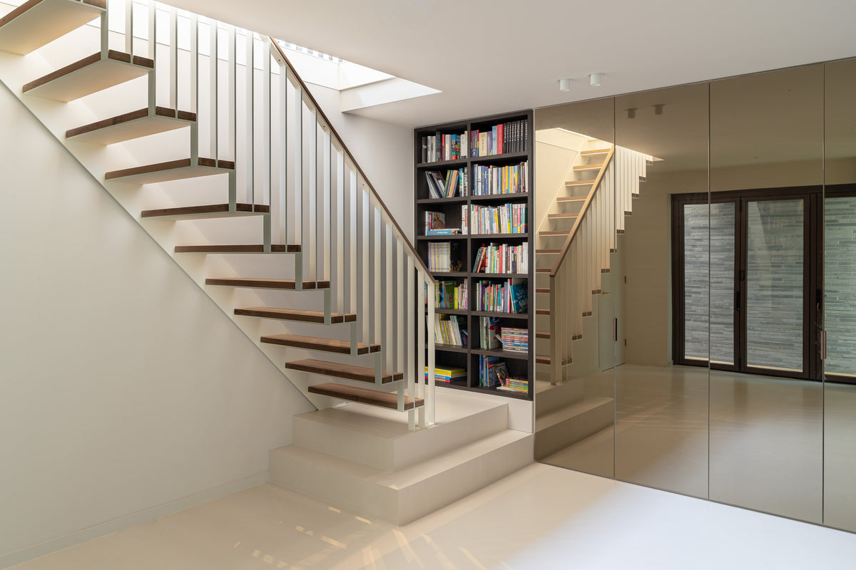 Open trap met houten treden, witte balustrade en een boekenkast naast een spiegelwand