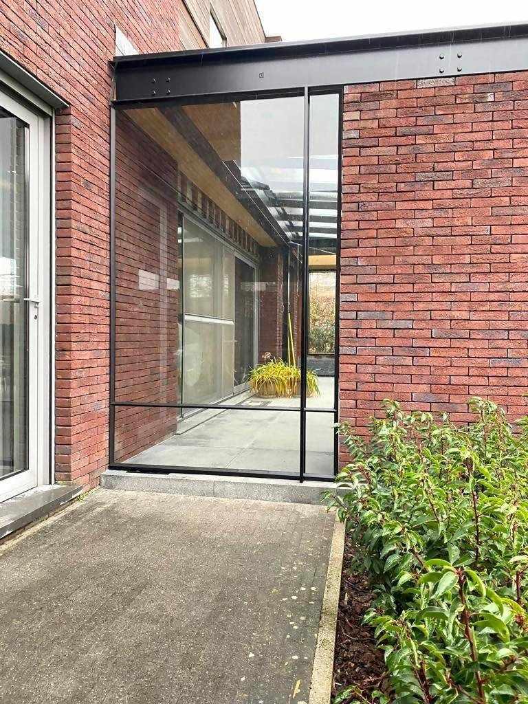 Stalen scheidingswand binnenplaats-Stalendeurenhuys-binnentuin overkapping,buitenruimte met glaswand,glazen scheidingswand,industriële staalconstructie,maatwerk stalen wand,stalen scheidingswand,stalen taatsdeur,tuin,windvrije binnenplaats-Stalen industriële deur als scheidingswand-OBLY