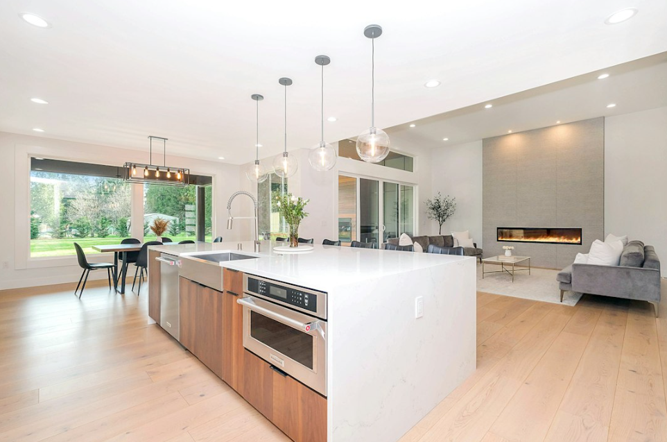 Open keuken met houten fronten, een wit keukeneiland en glazen hanglampen, verbonden met de eethoek en woonkamer met haard.