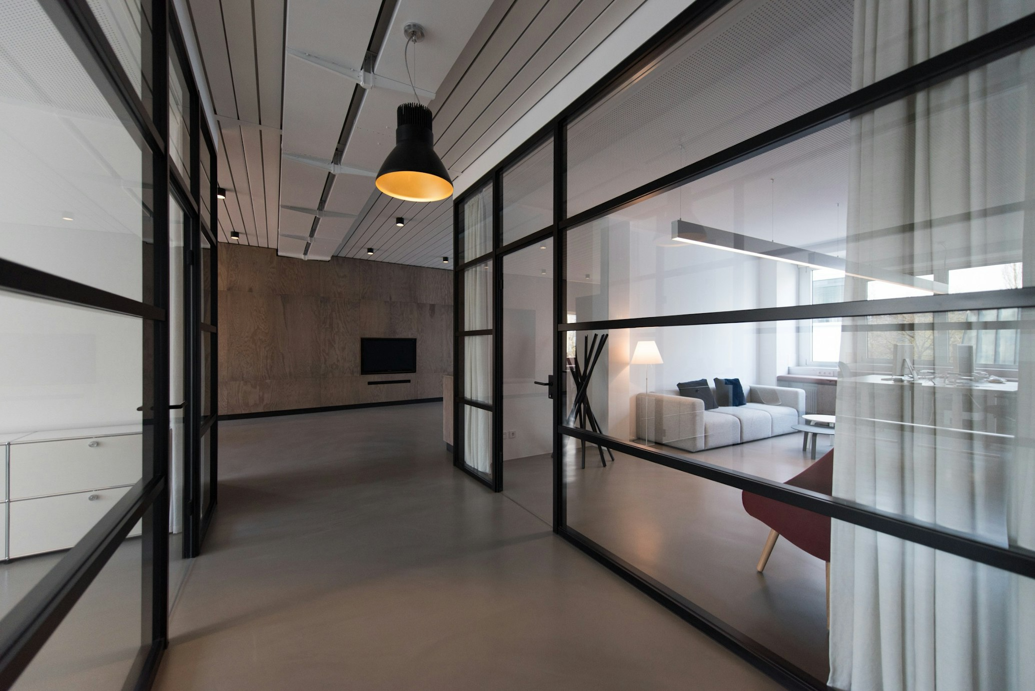 Moderne kantoorruimte met glazen wanden, zwarte metalen kozijnen, minimalistische inrichting en natuurlijke lichtinval door grote ramen.