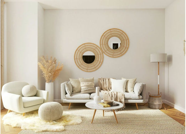 Stijlvol ingerichte woonkamer met ronde vormen, waaronder een gebogen fauteuil, ronde poef, ovale salontafel en twee ronde rotan spiegels aan de muur. Zachte aardetinten, natuurlijke materialen en een lichte, serene sfeer.