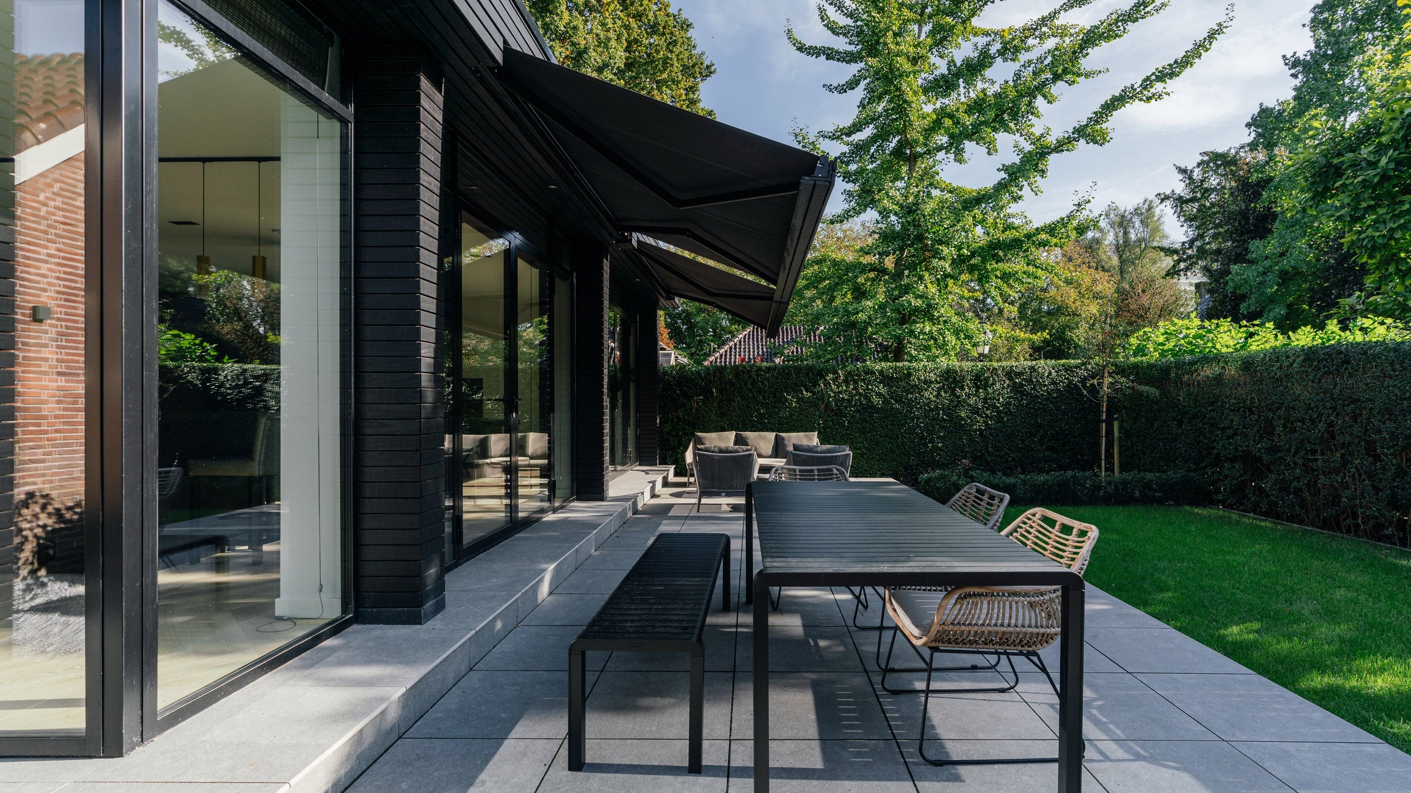 Modern terras en tuin na de totaalrenovatie met eigentijdse aanbouw en grote glaspartijen.