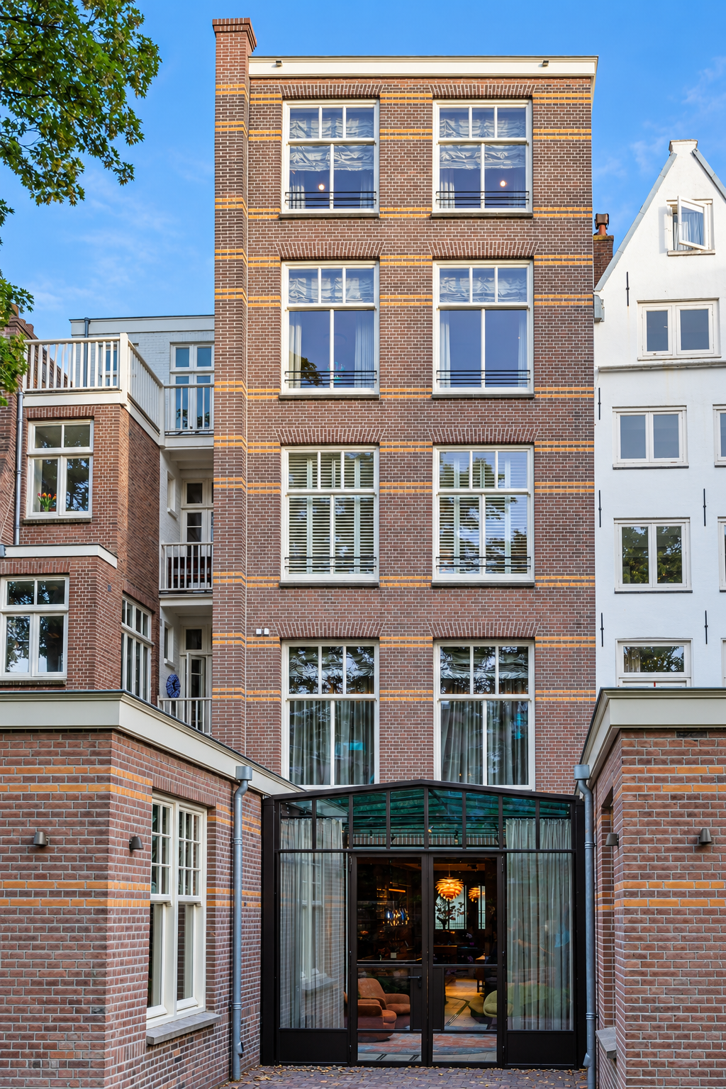 Bakstenen achtergevel met hoge ramen en een glazen serre na renovatie