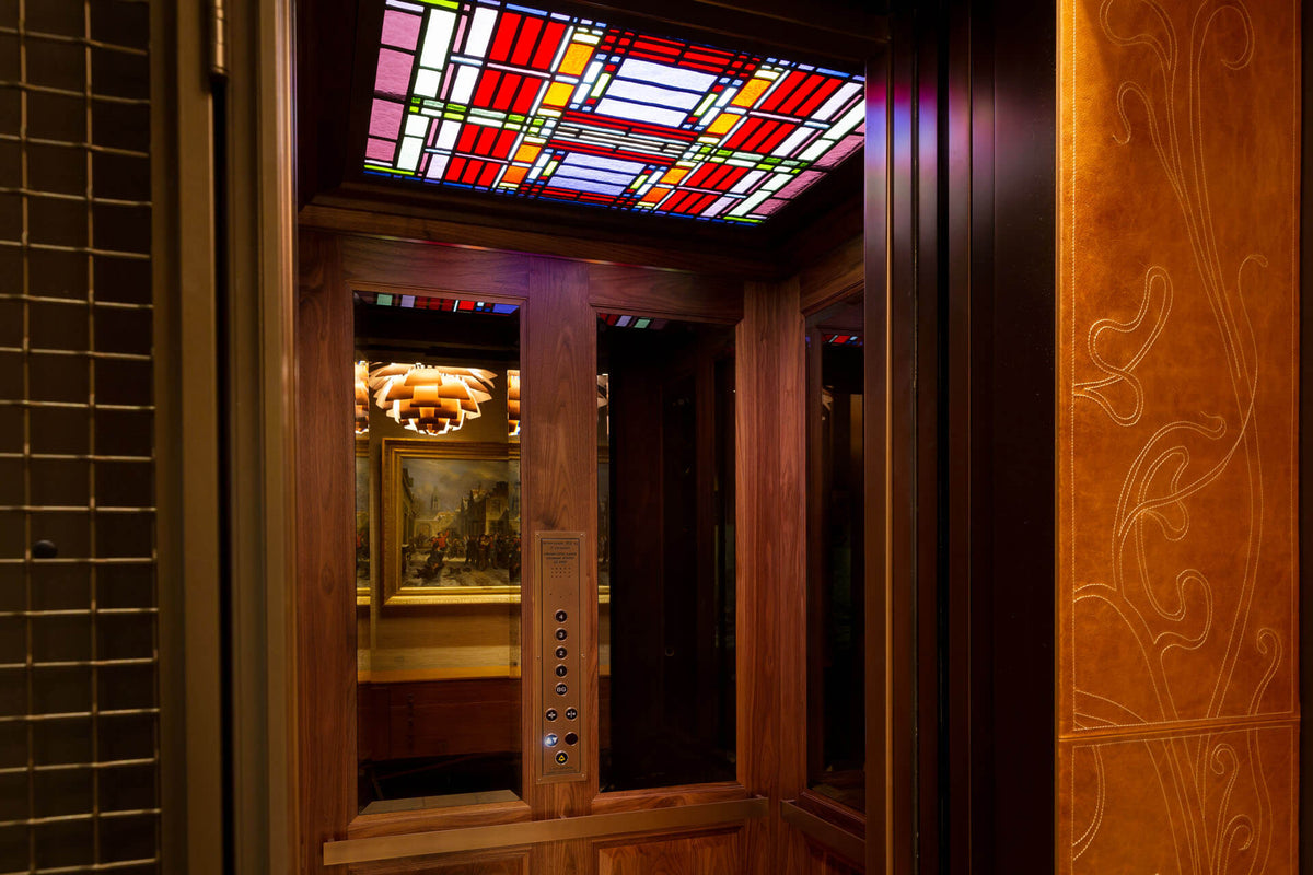 Huislift met houten panelen, spiegels en een kleurrijk glas-in-loodplafond na renovatie
