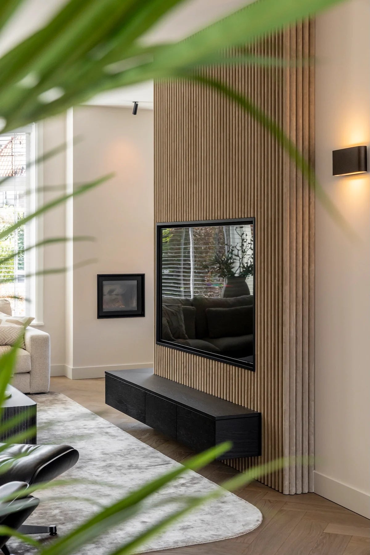After: maatwerk tv-wand in de vernieuwde woonkamer van een jaren ’30 woning in Breda, met verticale latten, geïntegreerde televisie en zwevend donker tv-meubel.