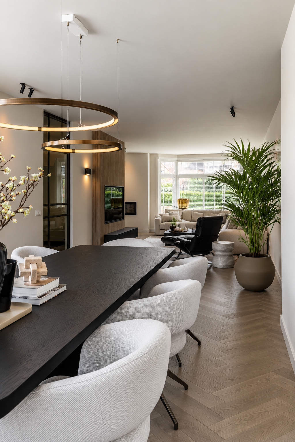 After: open eetkamer en woonkamer in een vernieuwde jaren ’30 woning in Breda, met lange eettafel, lichte eetkamerstoelen, houten visgraatvloer en zicht op de karakteristieke erker.