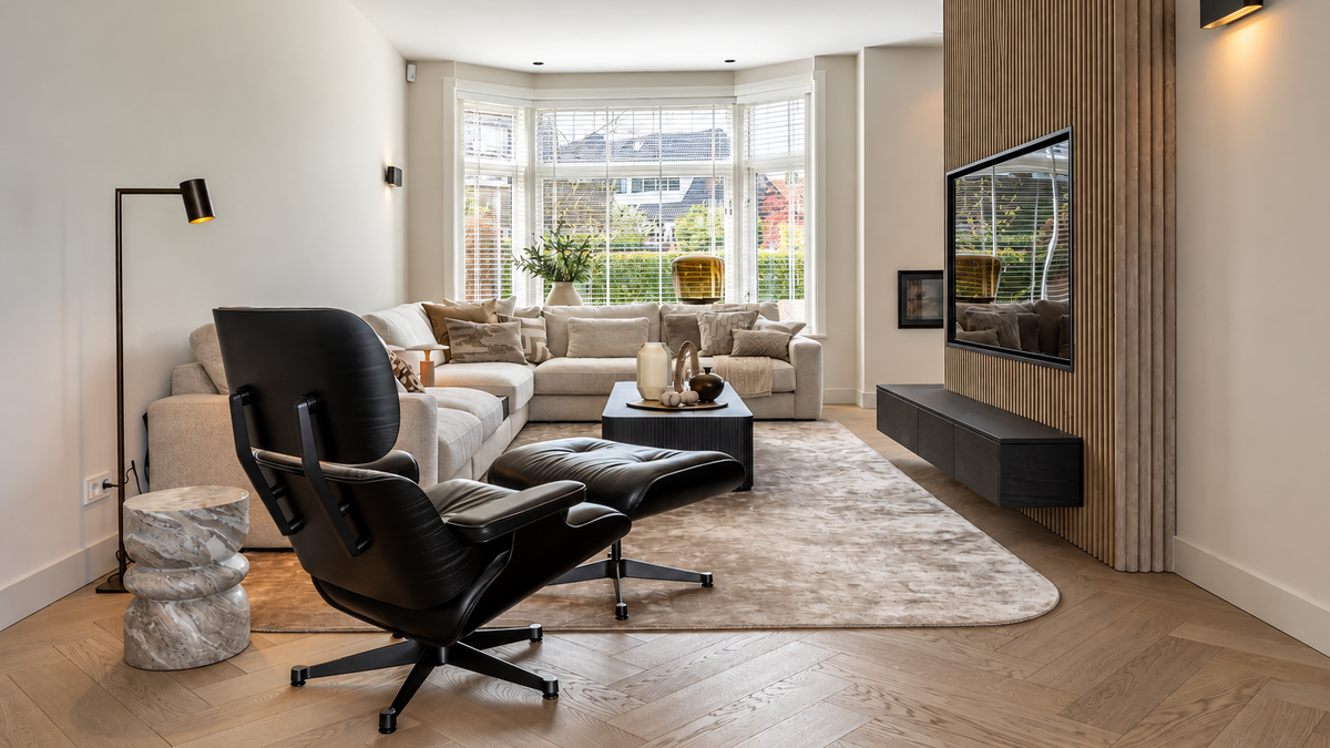 After: vernieuwde woonkamer van een jaren ’30 woning in Breda met karakteristieke erker, houten visgraatvloer, lichte zithoek en maatwerk tv-wand met verticale houten latten.