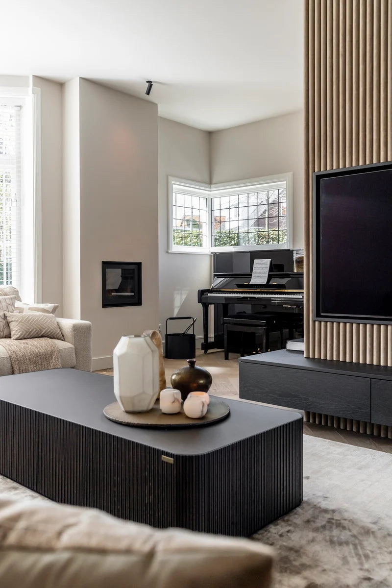 After: vernieuwde woonkamer van een jaren ’30 woning in Breda met maatwerk tv-wand, verticale latten, zwevend tv-meubel, zwarte piano en salontafel op maat.