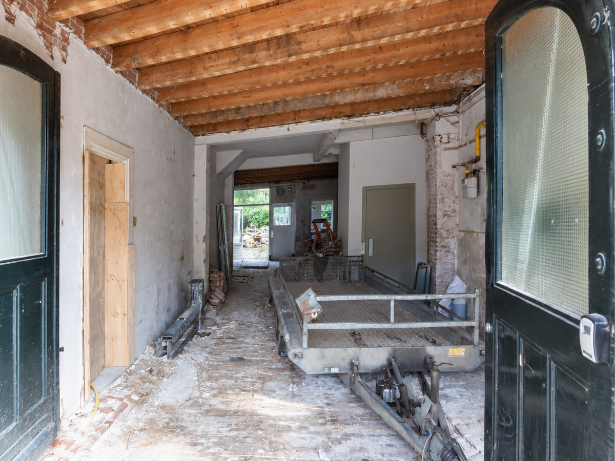 Doorgang tijdens renovatie met houten plafondbalken, dubbele deuren en een aanhanger