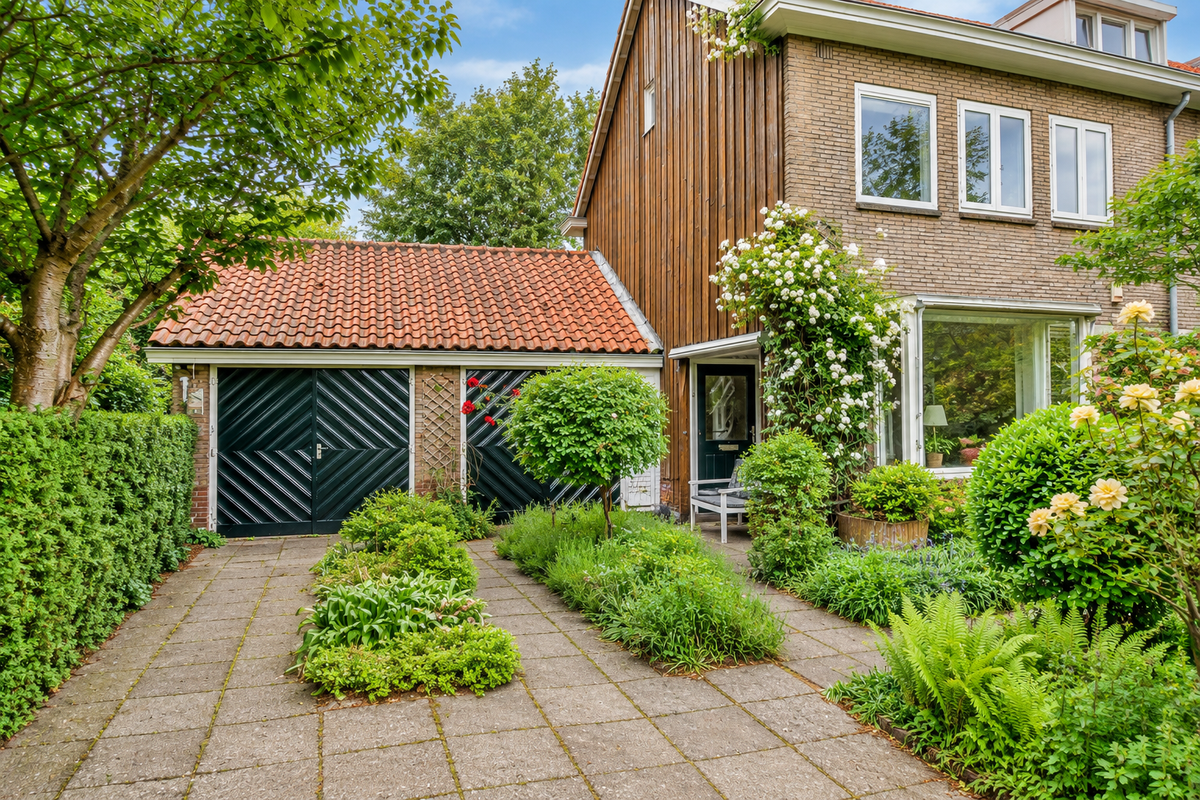 Woning vóór renovatie met houten gevelbekleding, een garage en een groene voortuin