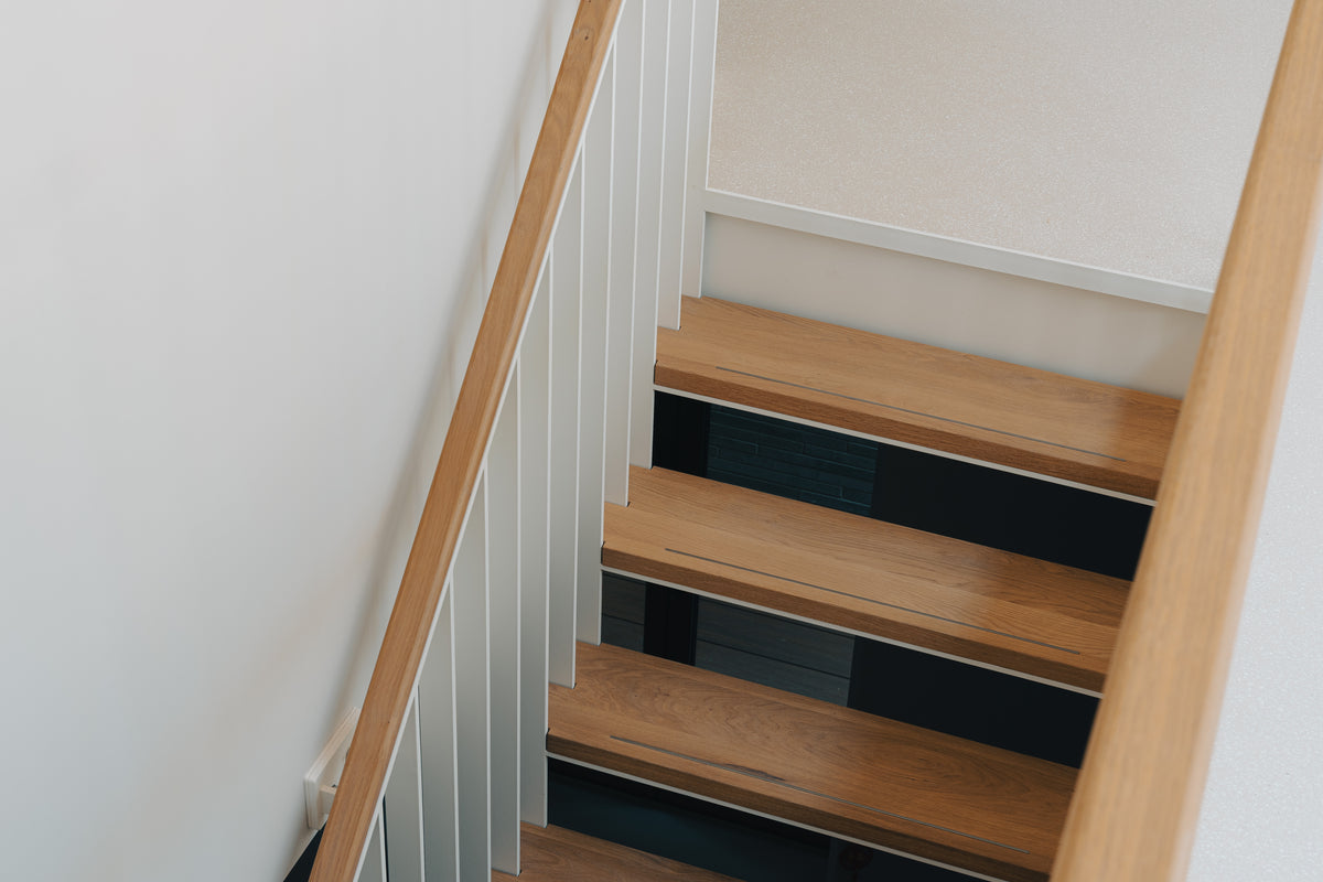 Detail van een open trap met houten treden, witte balustrade en houten leuningen