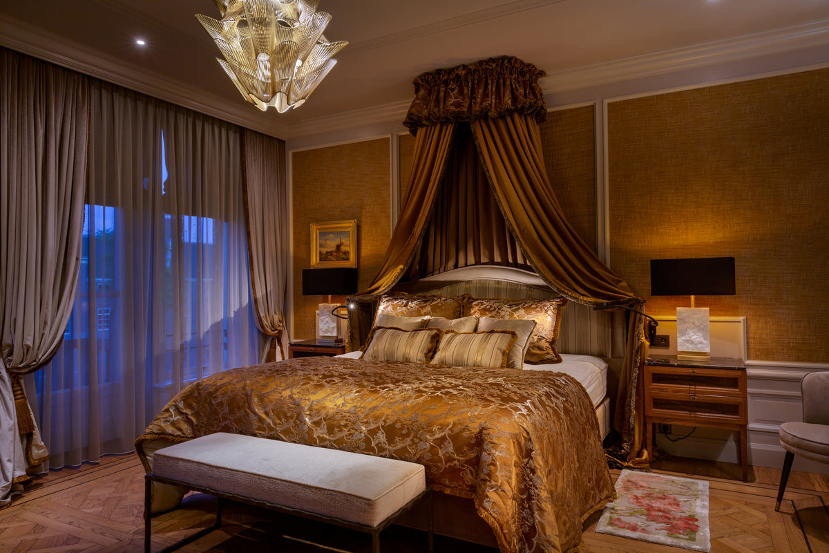 Klassieke slaapkamer in een grachtenpand aan de Herengracht in Amsterdam, met een hemelbed, goudkleurige stoffen, hoge gordijnen en een houten parketvloer.