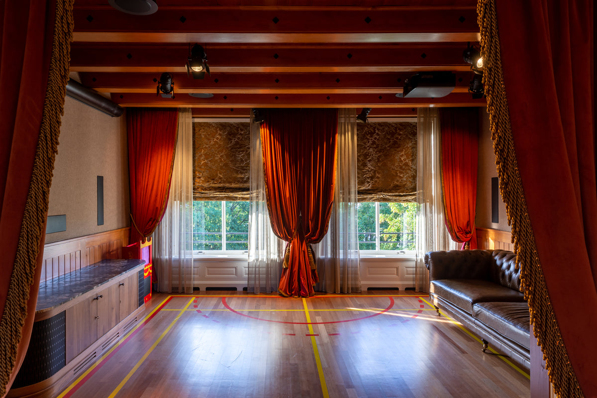 Theaterkamer in een monumentaal grachtenpand aan de Nieuwe Herengracht in Amsterdam, met rode gordijnen, houten balken en een houten vloer met sportbelijning.