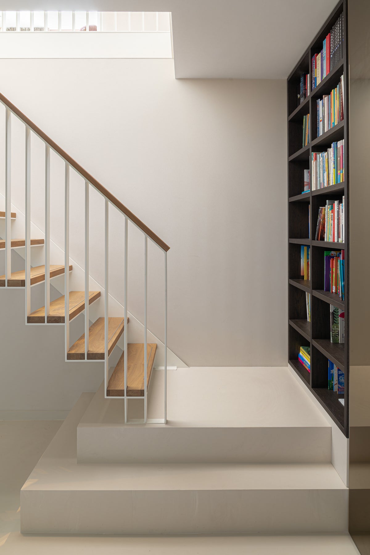 Trap met houten treden en witte balustrade naast een hoge donkerhouten boekenkast