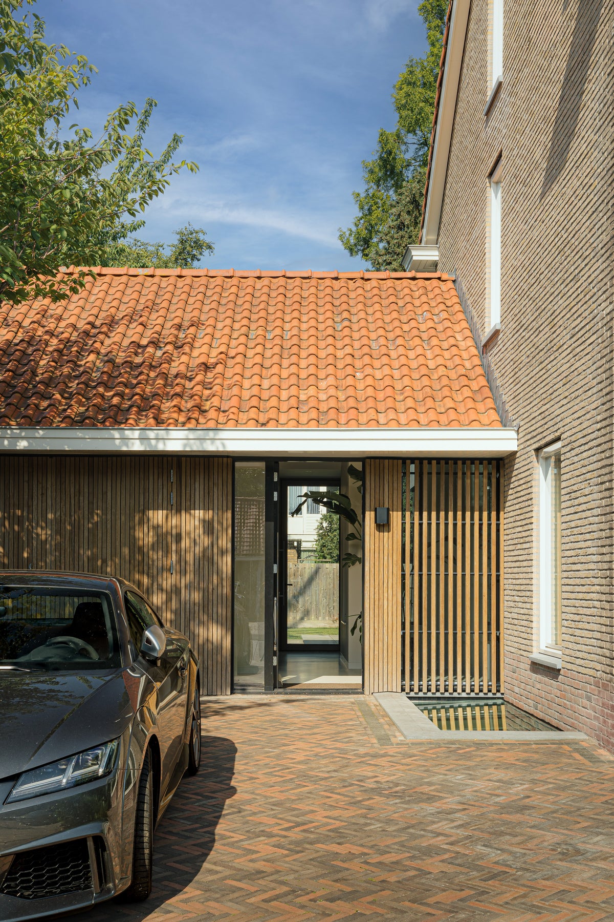 Glazen woningentree met houten gevelbekleding, verticale latten en rode dakpannen